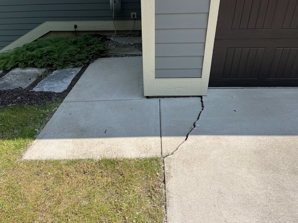 heaving crack in residential driveway concrete caused by soil movement and seasonal changes