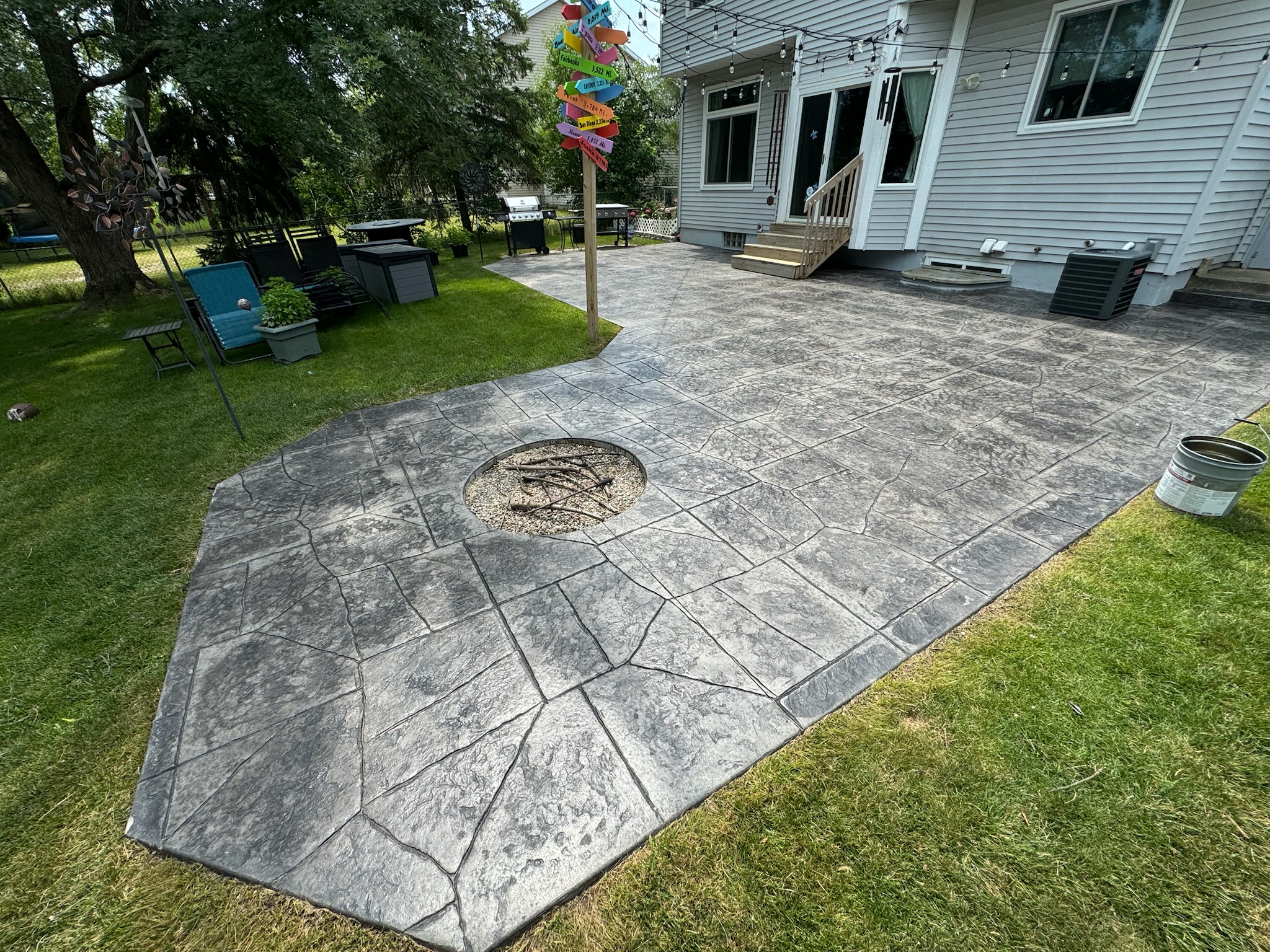 Decorative stamped concrete patio with a stone pattern and built-in fire pit, adjacent to a house and backyard.