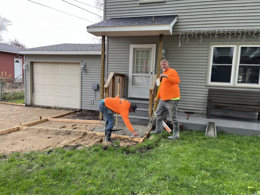 Construction crew setting forms and compacting sand base before concrete pour