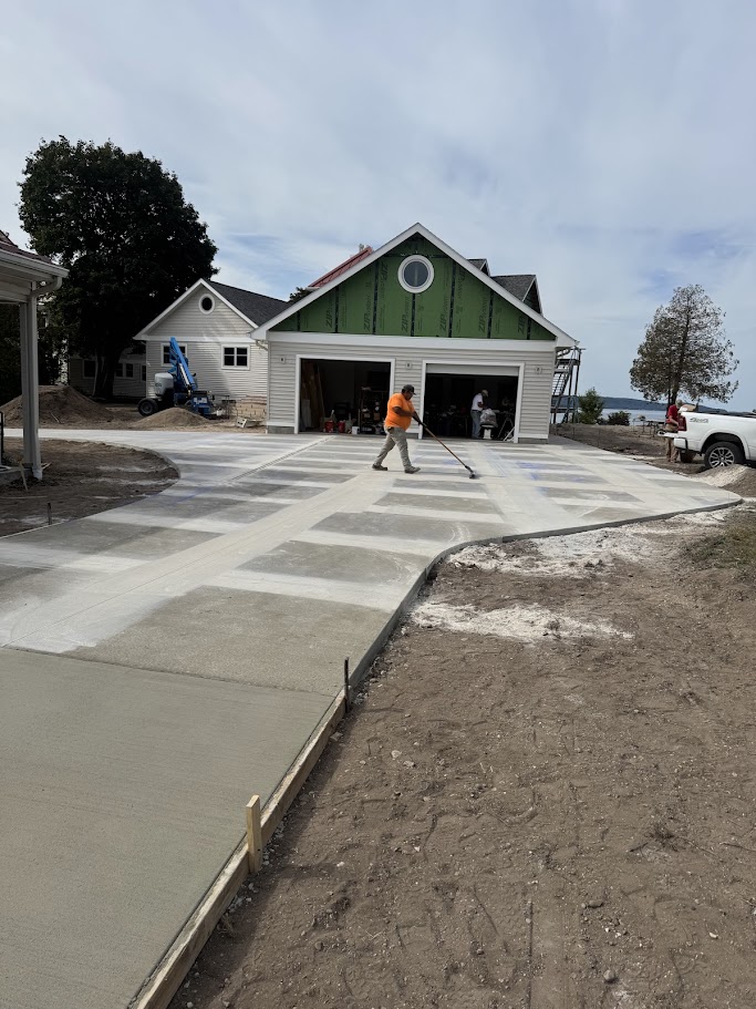 Worker using a long-handled trowel to finish a newly poured concrete driveway