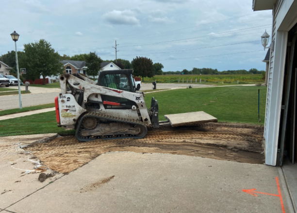 Skid steer removing old driveway material during concrete driveway replacement in Michigan